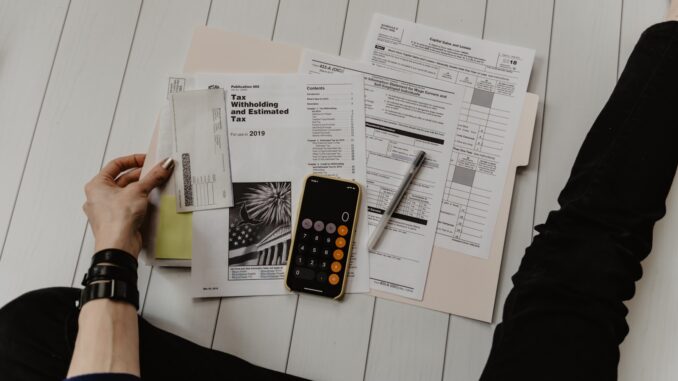 person holding paper near pen and calculator